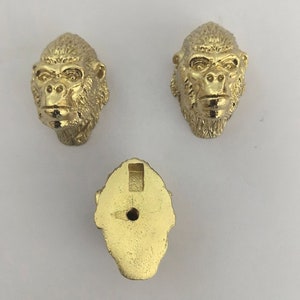 May include: Three gold-colored metal ornaments shaped like gorilla heads. The ornaments have a detailed design and are perfect for adding a touch of whimsy to any space.