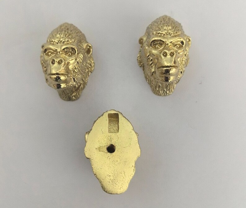 May include: Three gold-colored metal ornaments shaped like gorilla heads. The ornaments have a detailed design and are perfect for adding a touch of whimsy to any space.