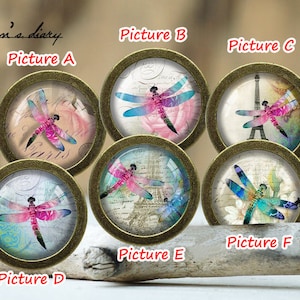 Könnte beinhalten: Sechs runde, goldfarbene, dekorative Schubladengriffe mit verschiedenen Libellenmotiven. Jeder Griff hat einen anderen Hintergrund, darunter Blumenmuster, eine Pariser Stadtlandschaft und ein Vintage-Briefdesign.