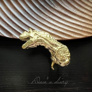 以下が含まれることがあります： 金色の恐竜の置物で、細部まで丁寧に作られています。置物は頭を上げて口を開けており、まるで咆哮しているようです。