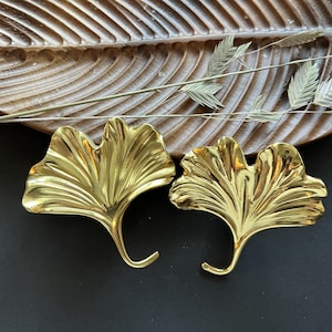 Puede incluir: Dos objetos decorativos de metal en forma de hoja de ginkgo de color dorado. Las hojas son detalladas y tienen una superficie texturizada.