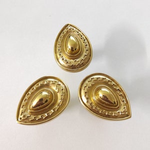 May include: Three gold-toned teardrop-shaped cabinet knobs with a decorative, concentric circle design.