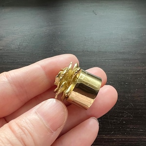 May include: A gold ring with a textured, flower-like design. The ring is made of metal and has a smooth, polished finish.