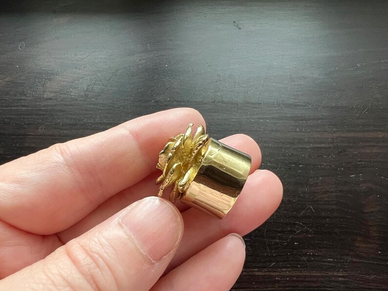 May include: A gold ring with a textured, flower-like design. The ring is made of metal and has a smooth, polished finish.