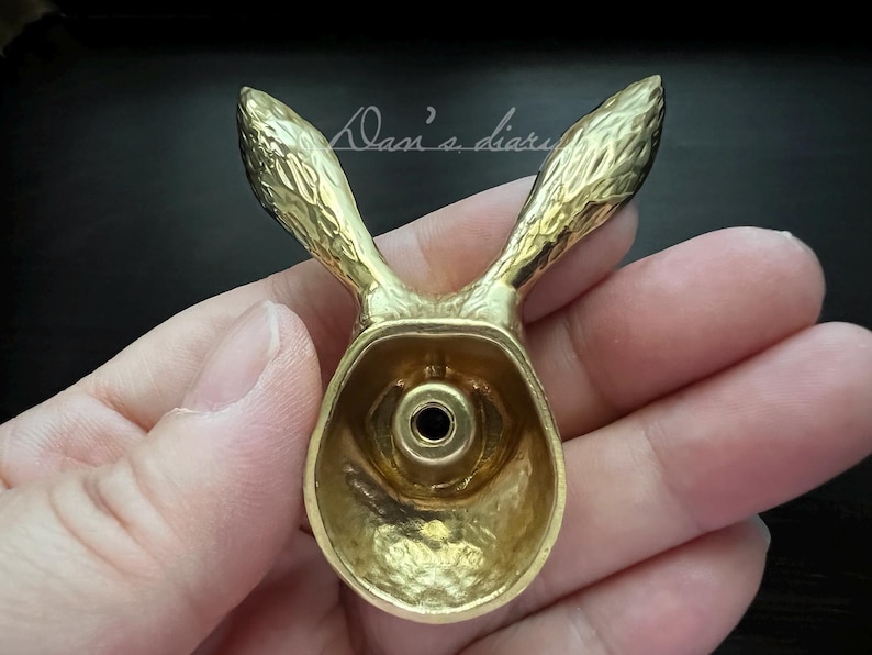 K&ouml;nnte beinhalten: Ein goldfarbener Wandhaken aus Metall in Form eines Kaninchenkopfes mit strukturierter Oberfl&auml;che. Der Haken ist so gestaltet, dass er wie ein Kaninchenkopf mit langen Ohren aussieht.