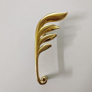 May include: Gold-toned metal door handle with a leaf design. The handle is shaped like a stylized leaf with multiple layers.