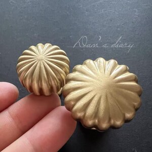 Puede incluir: Dos pomos de armario de metal dorado con un dise&ntilde;o acanalado con forma de flor.