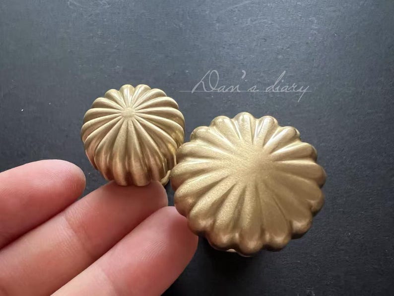 Puede incluir: Dos pomos de armario de metal dorado con un dise&ntilde;o acanalado con forma de flor.