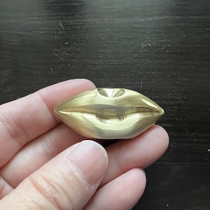 May include: A gold-colored metal sculpture of a pair of lips.