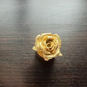May include: A gold-colored rose-shaped bottle stopper. The rose is detailed with intricate petals and a center bud.