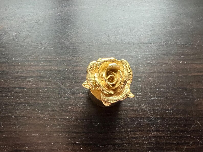 May include: A gold-colored rose-shaped bottle stopper. The rose is detailed with intricate petals and a center bud.