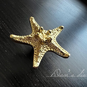 May include: Gold-toned metal starfish-shaped door knob or pull. The starfish has a textured surface.