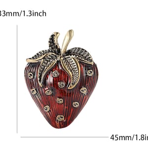 Op de afbeelding: Decoratieve aardbeivormige sieradendoos, rood met gouden details. De doos is 4,5 cm lang en 3,3 cm breed. Het ontwerp omvat gedetailleerde bladeren en een steel. Het oppervlak heeft een textuur met kleine, ronde details.