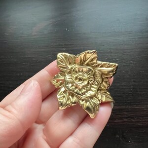 May include: A gold-toned metal flower brooch with a detailed rose design.