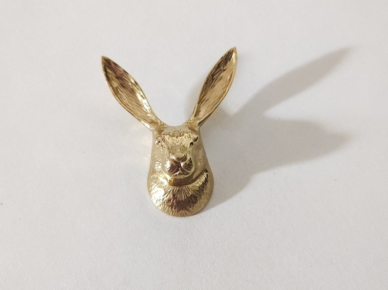 K&ouml;nnte beinhalten: Eine goldfarbene Metallskulptur eines Kaninchenkopfes mit langen Ohren.