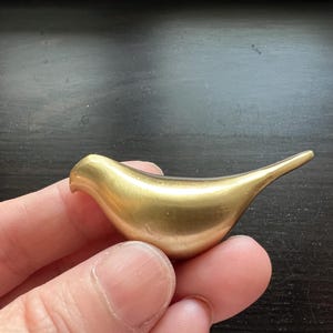 Pu&ograve; includere: Una piccola scultura a forma di uccello di colore dorato. La scultura &egrave; liscia e ha una forma arrotondata.