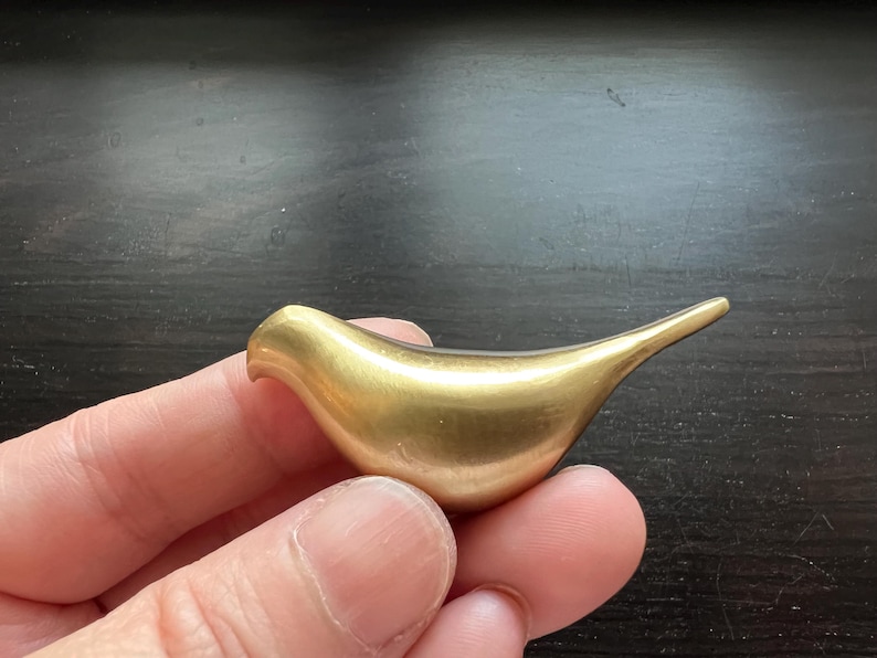 Pu&ograve; includere: Una piccola scultura a forma di uccello di colore dorato. La scultura &egrave; liscia e ha una forma arrotondata.