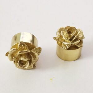 May include: Two gold-colored metal bottle stoppers with a rose design. The stoppers are cylindrical with a rose on top.