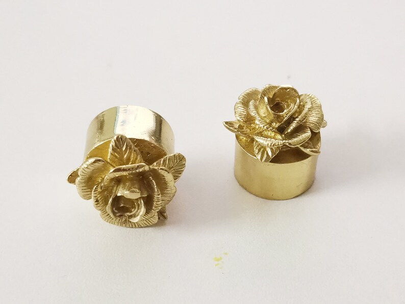 May include: Two gold-colored metal bottle stoppers with a rose design. The stoppers are cylindrical with a rose on top.