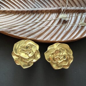 May include: A pair of gold-tone flower-shaped earrings. The earrings are made of metal and have a detailed design.