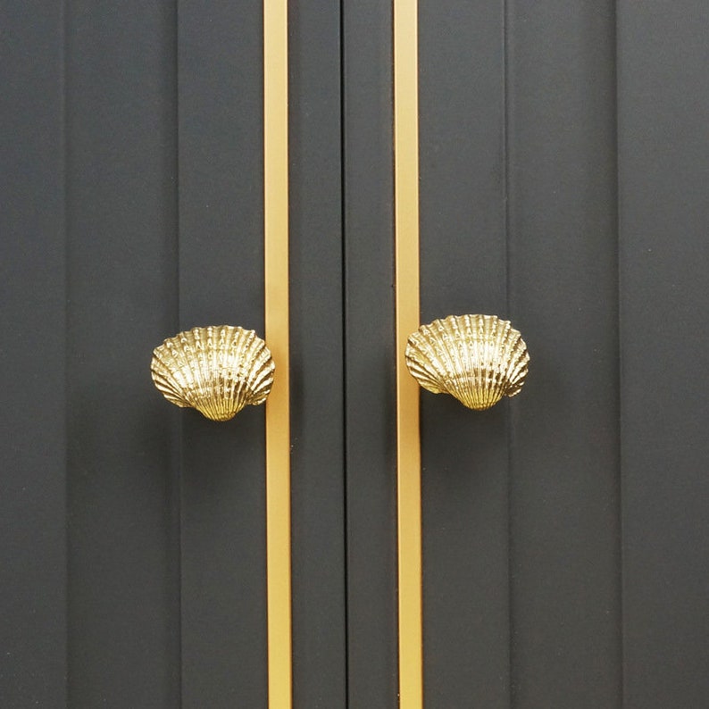 May include: Two gold shell-shaped cabinet door pulls on a black cabinet with gold trim.