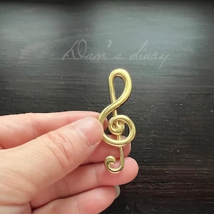 May include: A gold-coloured treble clef music note charm. The charm is a decorative piece of jewellery.