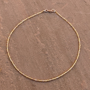 Gold tiny bead necklace against pinky Indian paving slab.