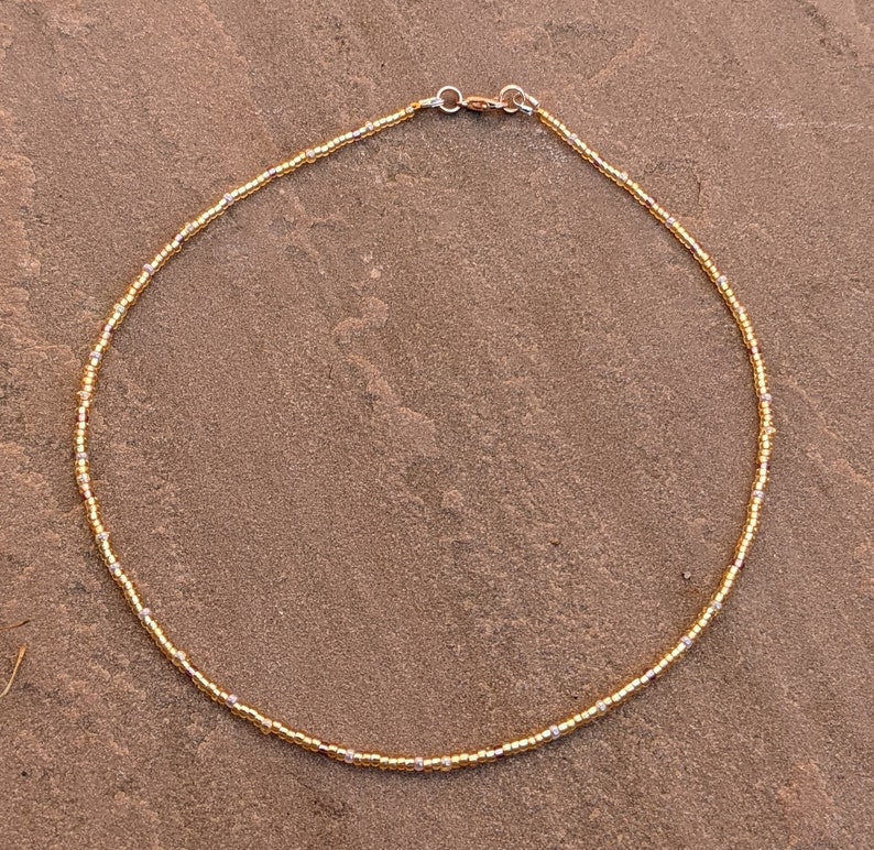 Gold tiny bead necklace against pinky Indian paving slab.