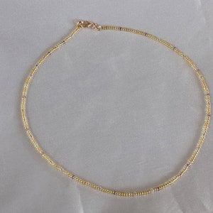 Gold tiny bead necklace on white fabric background in natural light.