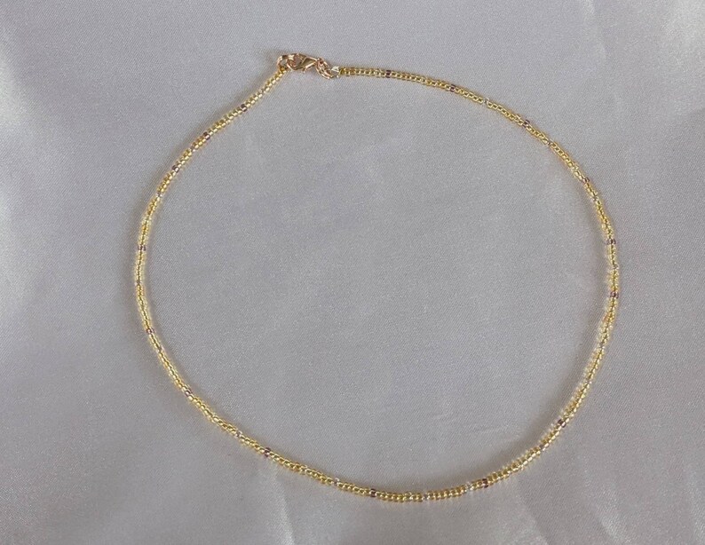 Gold tiny bead necklace on white fabric background in natural light.