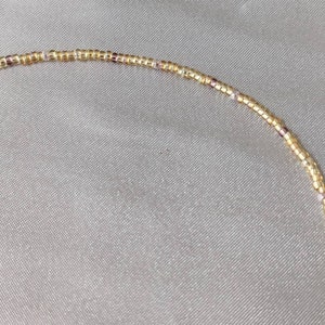 Close up of tiny gold bead necklace that shows the amethyst coloured beads speckled throughout to add detail and depth to the overall necklace.