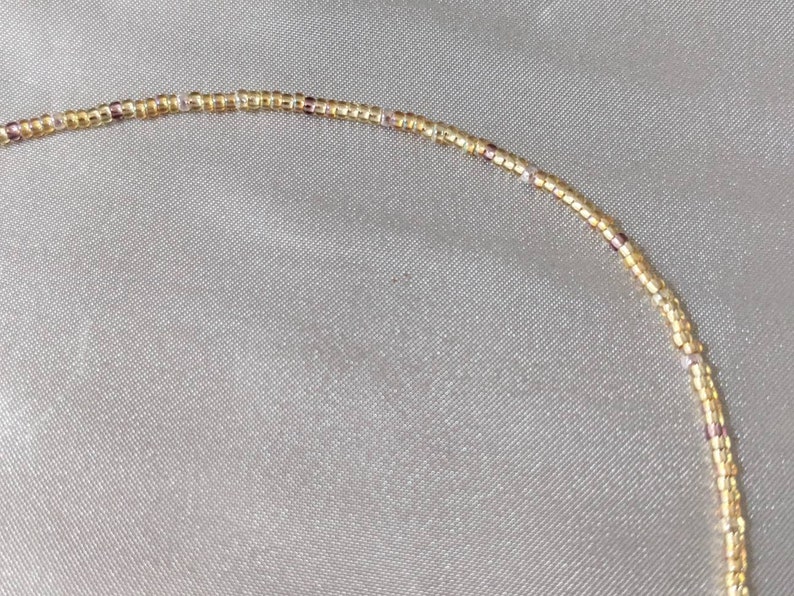 Close up of tiny gold bead necklace that shows the amethyst coloured beads speckled throughout to add detail and depth to the overall necklace.