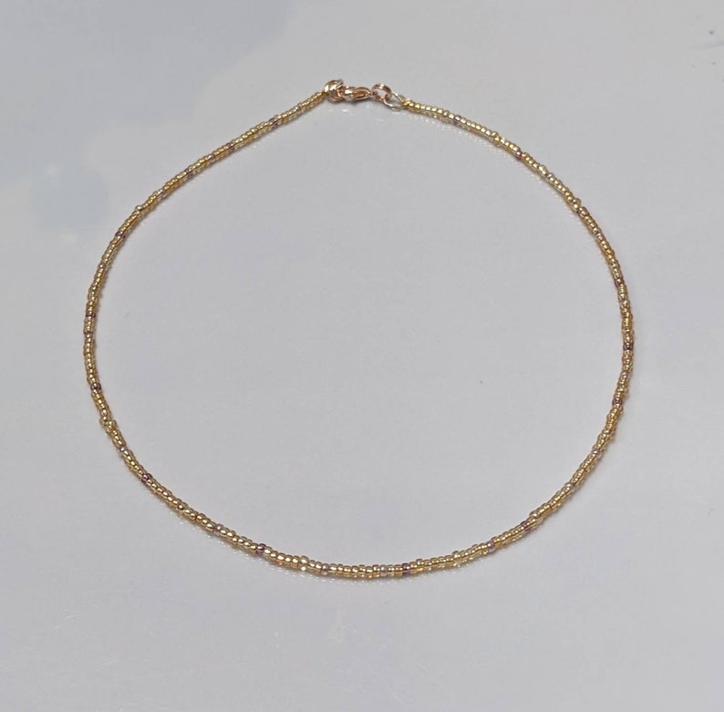 Gold bead necklace laid out on white background.