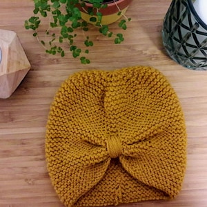 Puede incluir: Un turbante de punto amarillo mostaza con un lazo anudado en la parte superior.