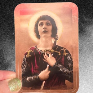 Puede incluir: Una imagen de estilo vintage de una mujer con una túnica roja y dorada, sosteniendo una espada, con un halo detrás de su cabeza.