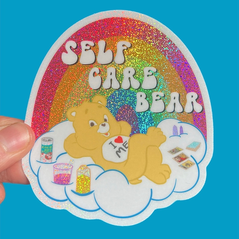 May include: A rainbow glitter sticker featuring a Care Bear with the text "Self Care Bear" and "I &hearts; Me" on its chest. The bear is lying on a cloud with a can of coconut milk, a glass of pink liquid, and a bottle of yellow liquid.