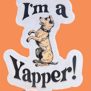 May include: A white sticker with a black outline features a cartoon dog standing on its hind legs. The dog is brown and white with a black collar. The text "I'm a Yapper!" is written in black letters.