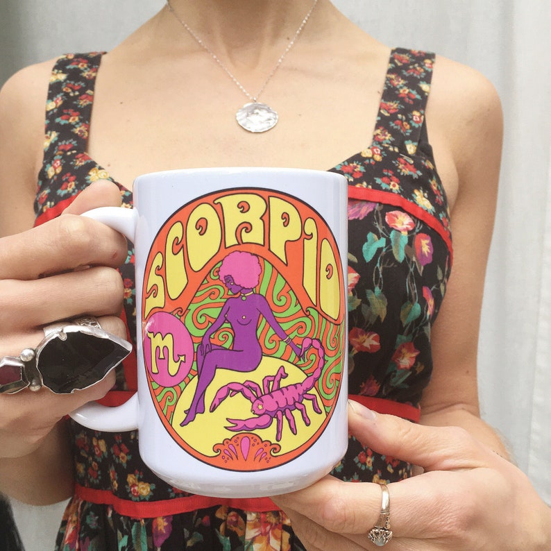 May include: White ceramic mug with a colorful graphic of a woman and a scorpion. The graphic includes the word "Scorpio" in a psychedelic font.