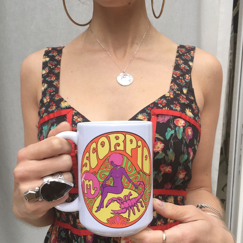 May include: White ceramic mug with a colorful graphic of a woman with a scorpion and the word "Scorpio" in a psychedelic font.
