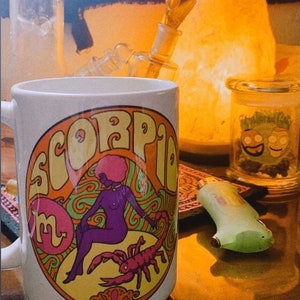 May include: White ceramic mug with a colorful illustration of a woman with a scorpion. The mug has the word "Scorpio" written in a retro font around the illustration. The text "I love it" and "Thank u" are written on the image.