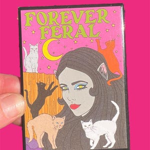May include: A pink and green illustrated patch with the text "FOREVER FERAL" and a woman with cat ears surrounded by five cats.