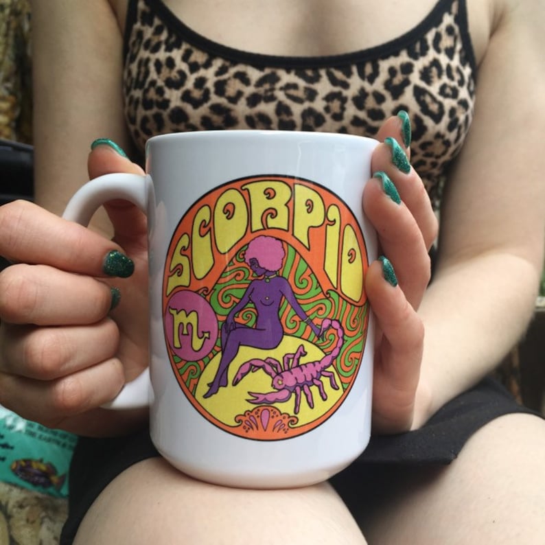 May include: White ceramic mug with a colorful graphic of a woman with a scorpion. The graphic says "Scorpio" in a retro font.
