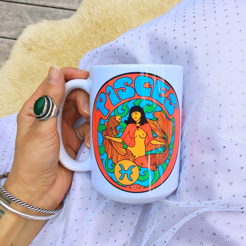 May include: White ceramic mug with a colorful graphic of a mermaid with the word "Pisces" in a retro font.