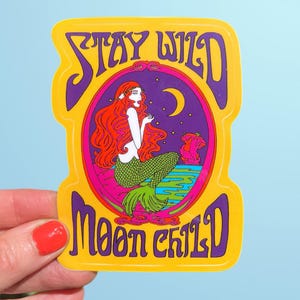 May include: A yellow sticker with the words "STAY WILD MOON CHILD" in purple. The sticker features a mermaid with red hair and a green tail inside a purple oval. A crescent moon is also visible.