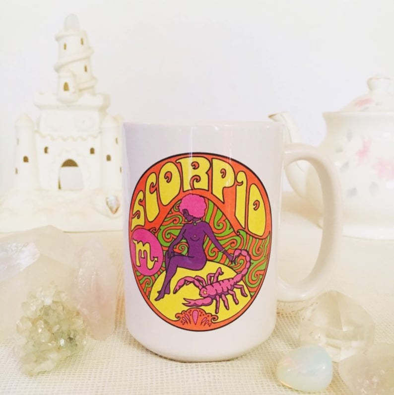 May include: White ceramic mug with a colorful graphic of a woman sitting on a scorpion with the word "Scorpio" in a psychedelic font.