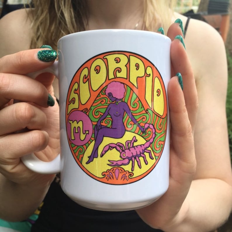 May include: White ceramic mug with a colorful graphic of a woman sitting on a scorpion with the word "Scorpio" in a psychedelic font.