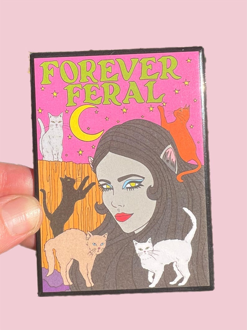 May include: A pink and green illustrated pin with the text "FOREVER FERAL" and a woman with cat ears surrounded by cats.