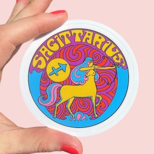 Puede incluir: Una pegatina circular blanca con una ilustración colorida del signo del zodíaco Sagitario. La ilustración presenta un centauro con arco y flecha, rodeado de patrones en espiral en tonos de morado, azul, rojo y amarillo. La palabra "Sagitario" está escrita en una fuente retro alrededor del borde del círculo.