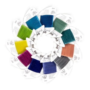 May include: A circular arrangement of twelve spools of Frosty Rays metallic polyester thread in various colors, including lime, teal, blue, purple, and copper. Each spool features a white label with product details and 5.5 meters of thread.