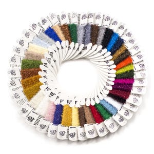 May include: A circular color swatch fan featuring numerous samples of fuzzy, textured yarn in a wide spectrum of colors including white, yellow, orange, red, pink, purple, blue, green, brown, gray, and black, each attached to a white paper tag.